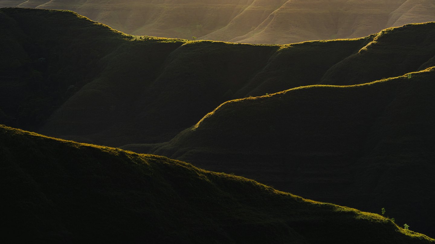 Goldene Sonnenstrahlen beleuchten die Spitzen von sanft geschwungenen Hügeln.