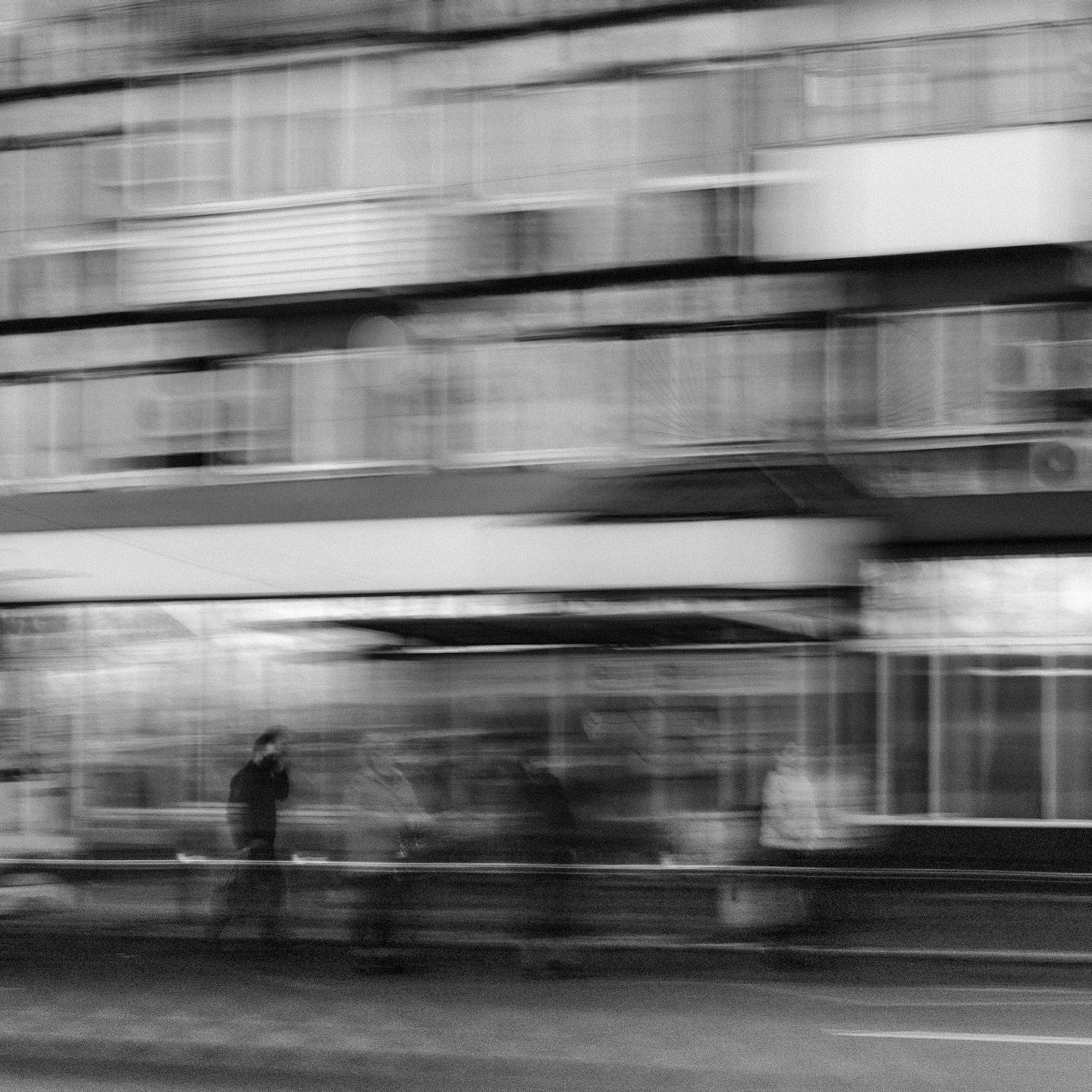 Verschwommene Gestalten gehen an einer Gebäudefassade in einer Stadt vorbei.