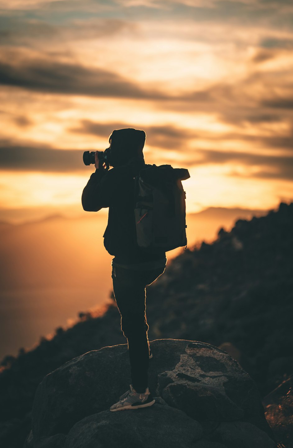 Fotograf vor einem lebhaften Sonnenuntergang über Bergen als Silhouette.